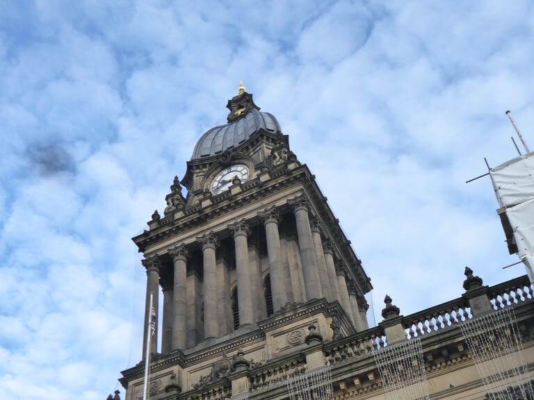 The clock tower of Leeds Town Hall against a sunny sky.